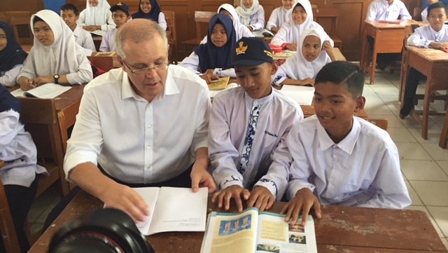 Scott Morrison at a desk with two Indonesian boys looking at a text book.