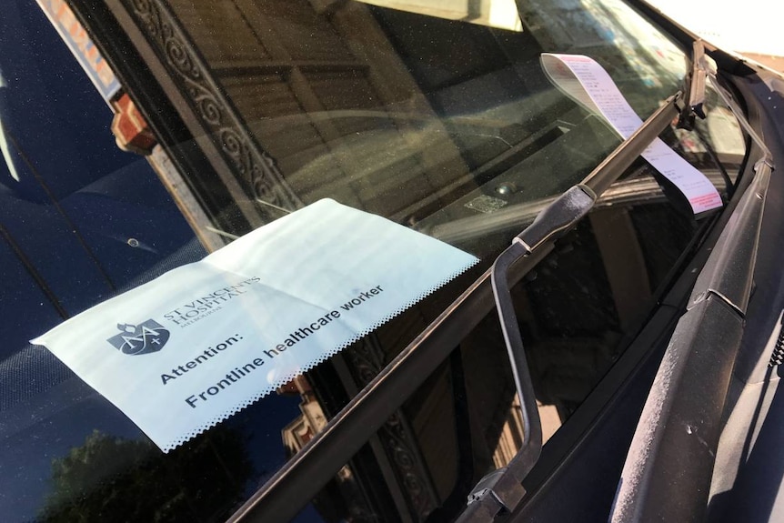A notice in a car windscreen saying frontline healthcare worker from St Vincent's Hospital next to an official warning ticket.