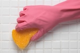 A close-up image of a hand with a rubber glove on it, holding a sponge which is being used to scrub tiles