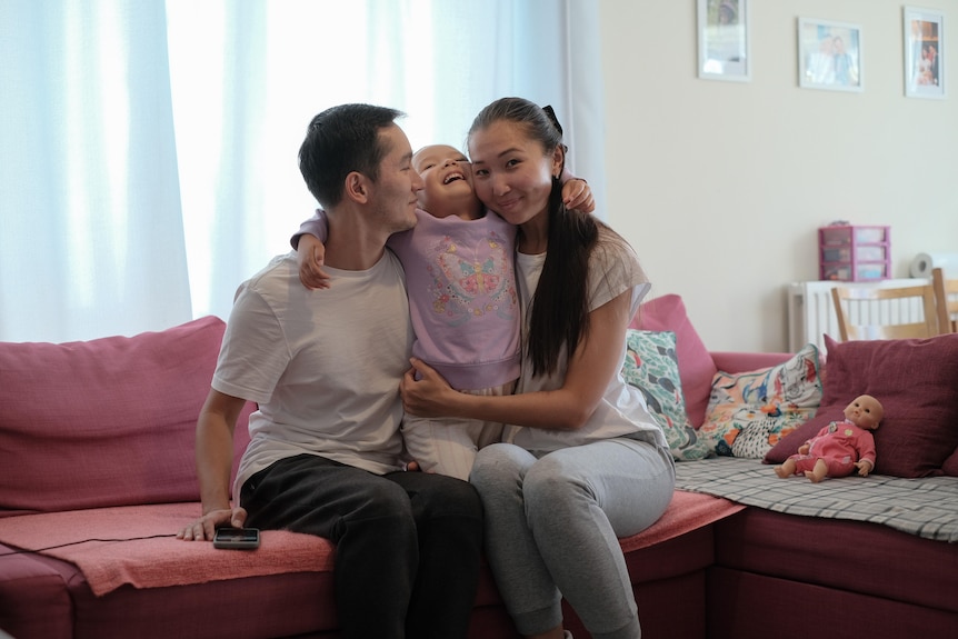 Togzhan Mussirova along with her husband and daughter laugh together on the couch