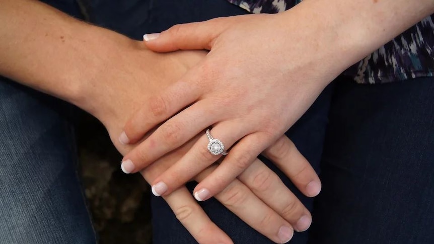 A women's sparkling diamond ring is clearly visible in this shot of a man and woman touching hands