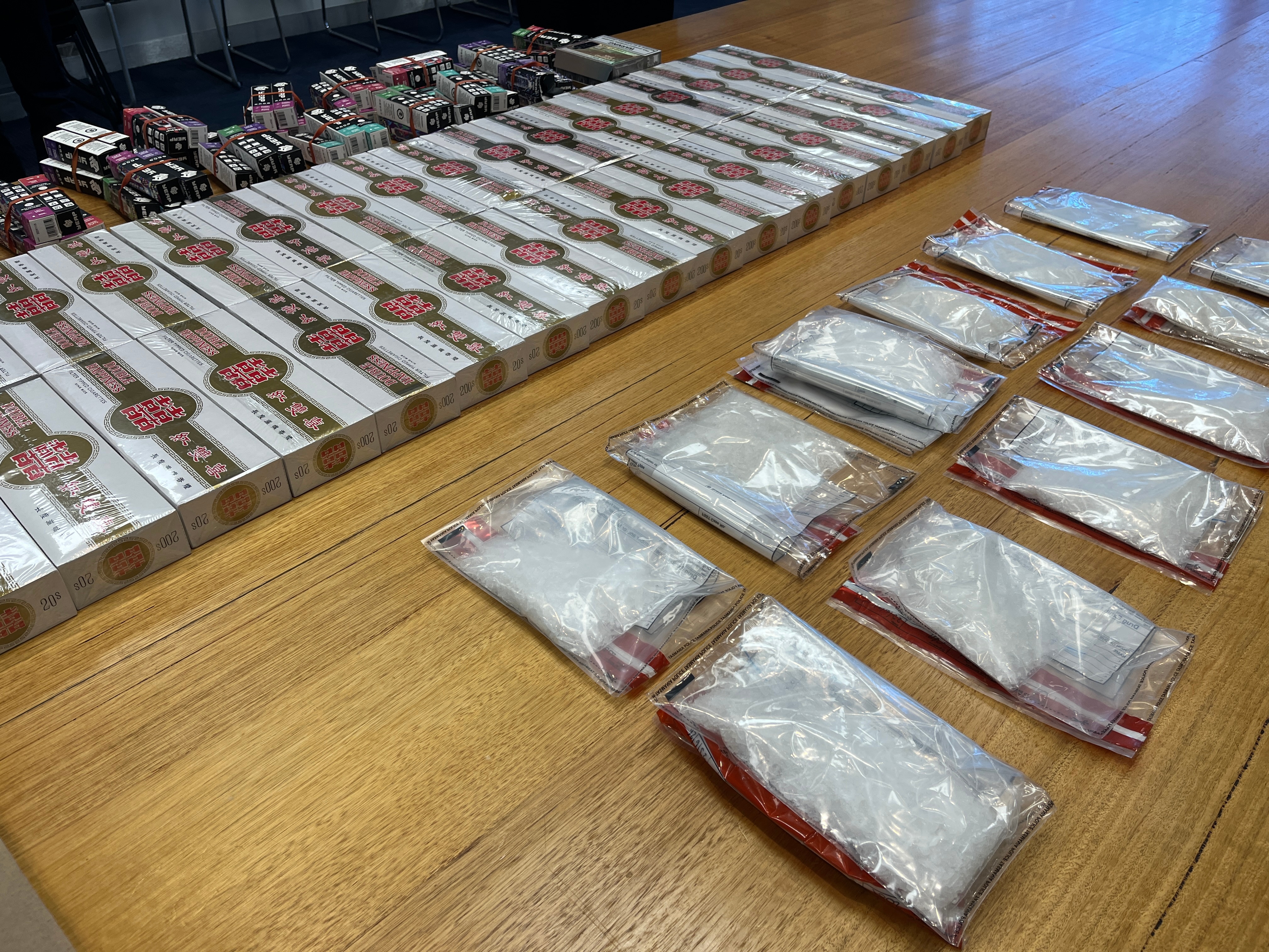 A large quantity of illicit drugs and tobacco on a wooden table.