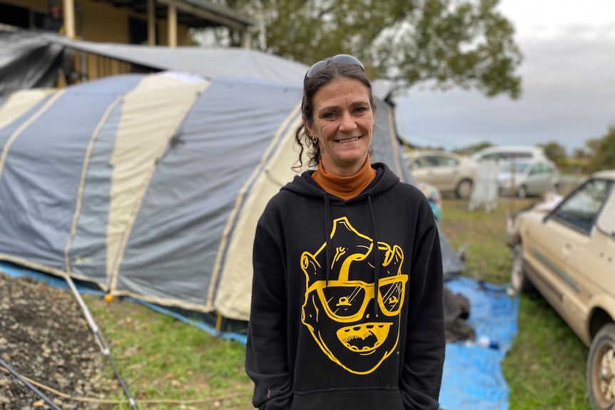 Woman wearing a black hoodie standing in front of a tent.