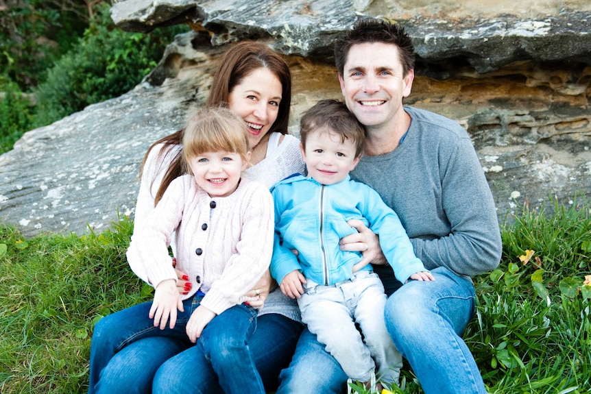 Two parents smile as they sit side by side with a young son and daughter in their laps.