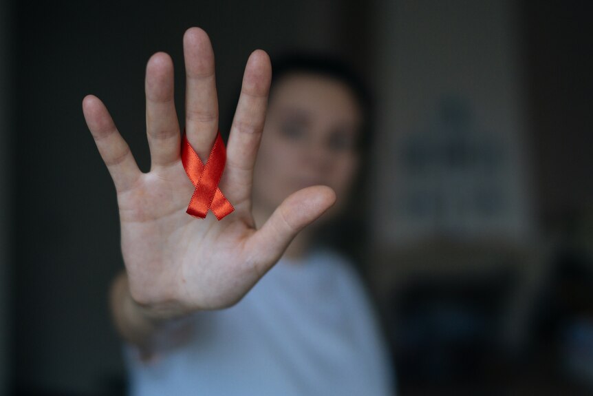 A woman holds out her hand with a red ribbon around in support of World Aids Day