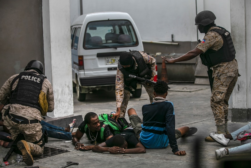 Des policiers en gilets pare-balles et camouflés arrêtent des hommes sur le terrain en Haïti 