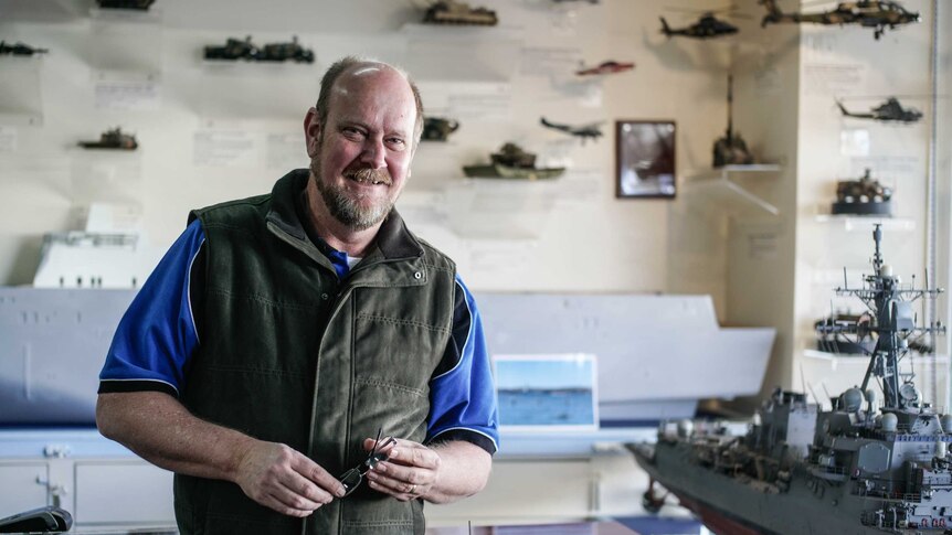 A man standing in front of model ships and vehicles