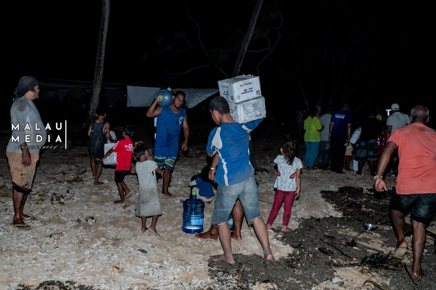 Tongans, young and old, collect supplies on beach after tsunami. 