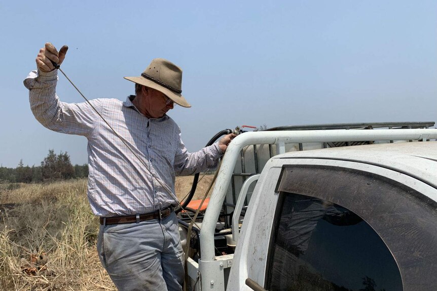 A man pulls the engine-starting cord on a device mounted on the back of a ute.