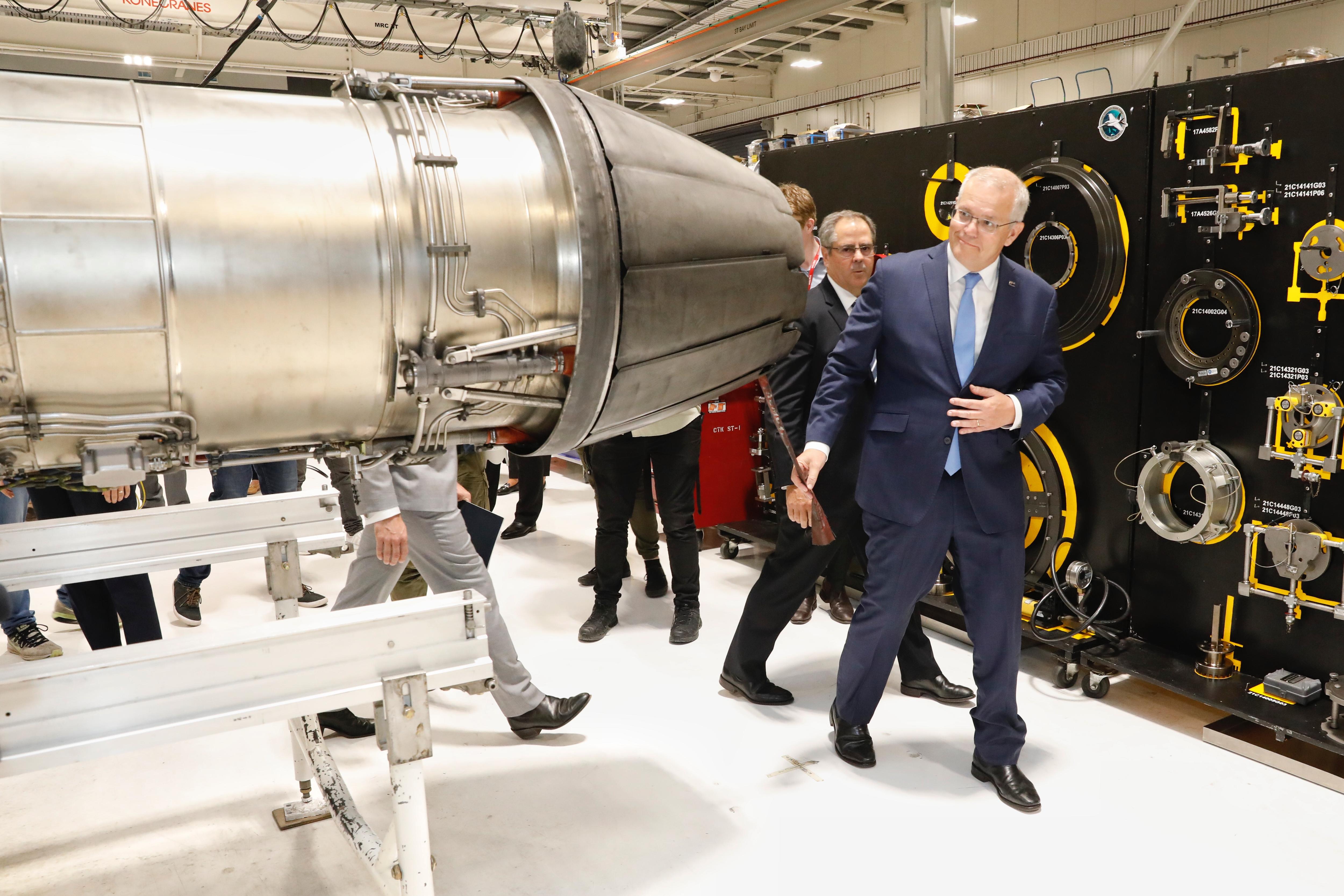 A man in a suit dodges around a piece of machinery shaped like a missle