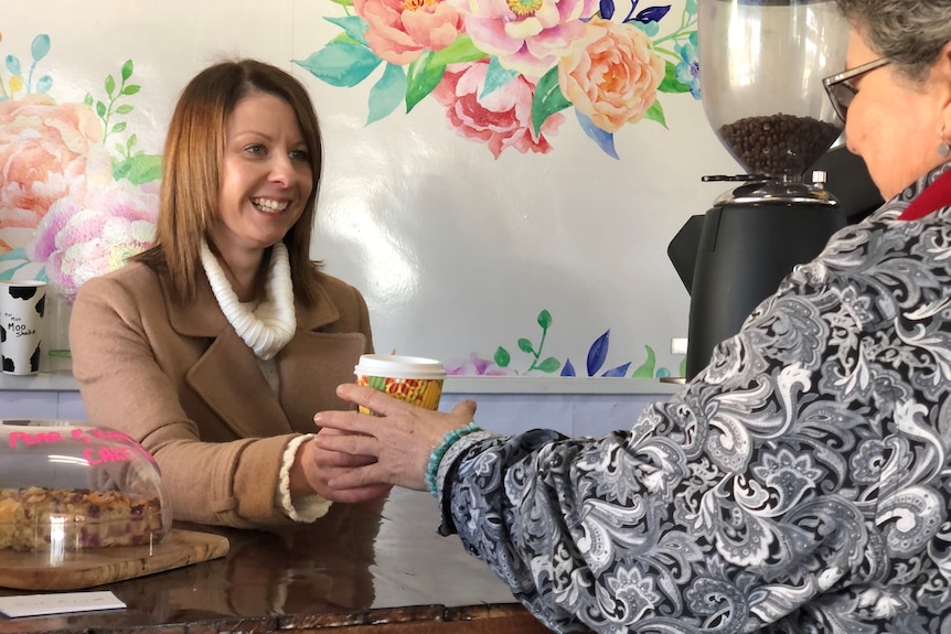 A female barista smiles as she hands a takeaway coffee to a customer