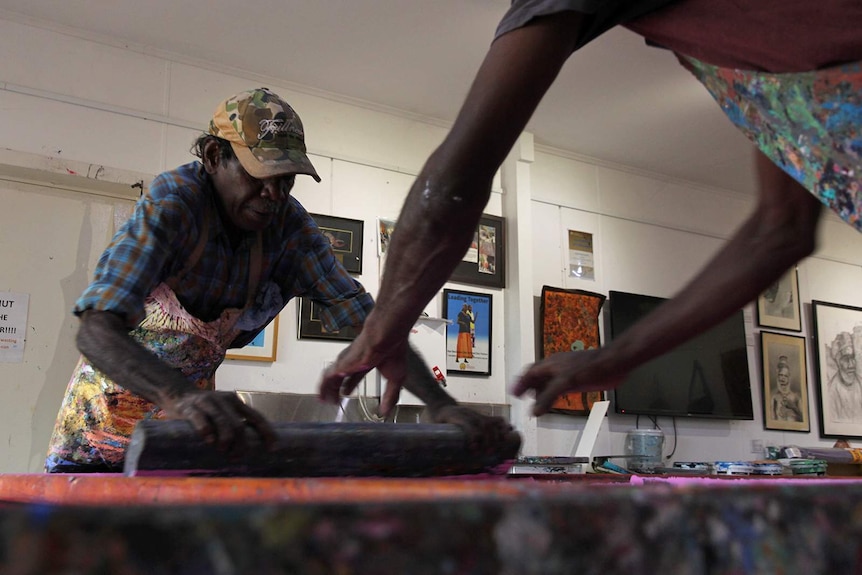 A photo of two screen printers adding designs to a piece of fabric in the Injalak Arts studio.