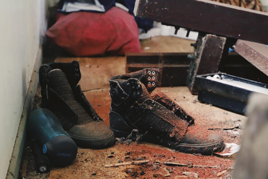 A close-up of the floor of a dirty house including dirty boots and a water bottle.