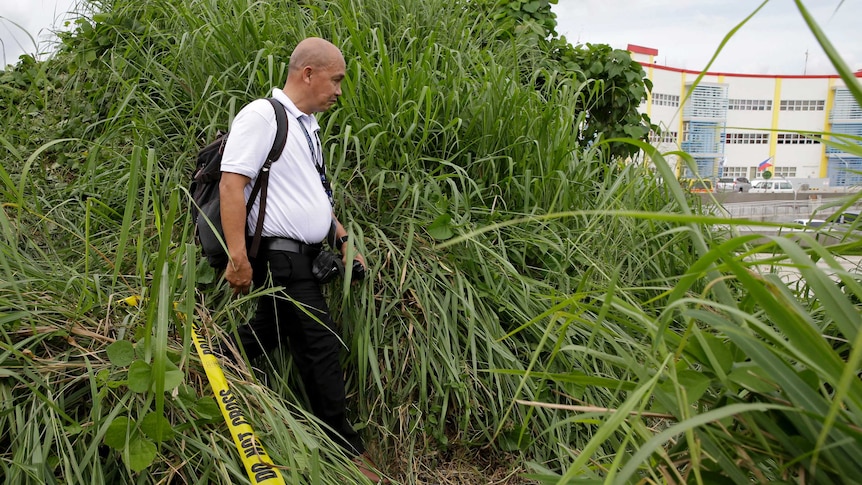 An investigator walks through a thick grassy area with police tape near him.