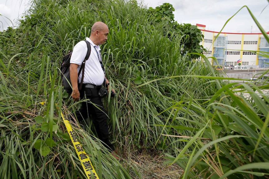An investigator walks through a thick grassy area with police tape near him.