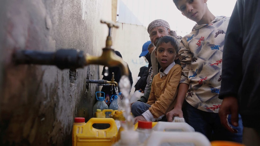 Sanaa residents group around a water tap with gasoline canisters to collect water provided by charities.