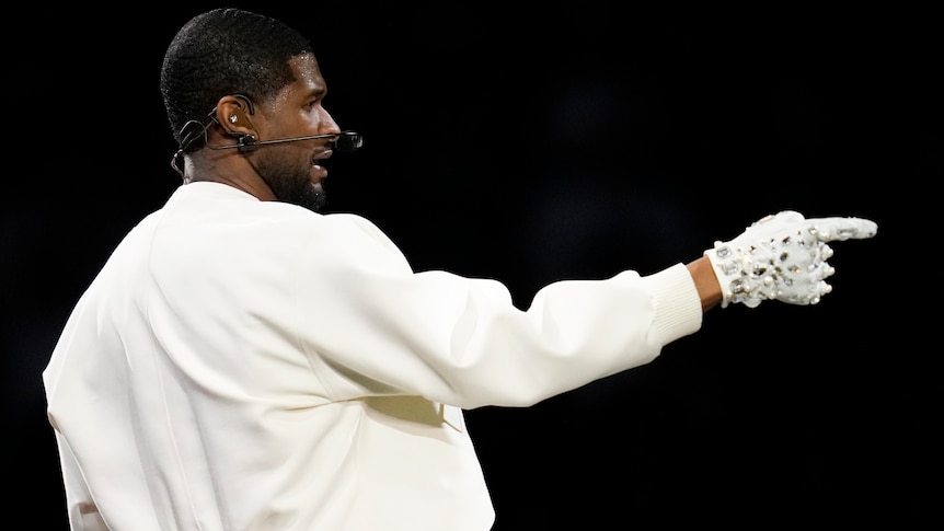 Usher pointing wearing white and a white diamond encrusted glove, side profile