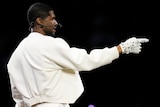 Usher pointing wearing white and a white diamond encrusted glove, side profile