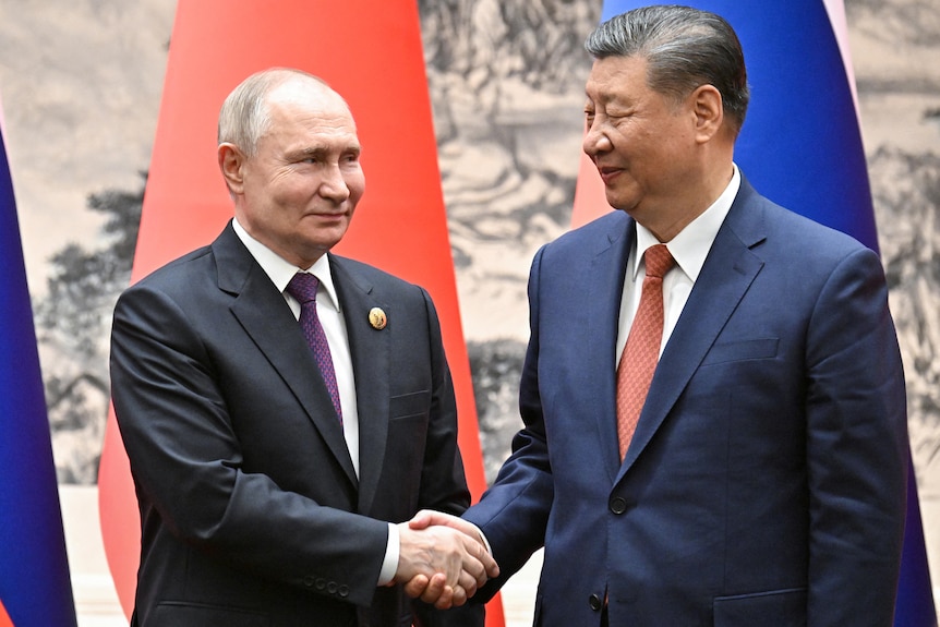 Vladimir Putin and Xi Jinping shake hands in front of Russia and China's flags