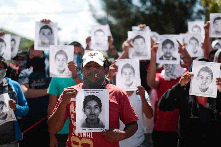Students from a teacher training college hold pictures of missing students outside building in Chilpancingo