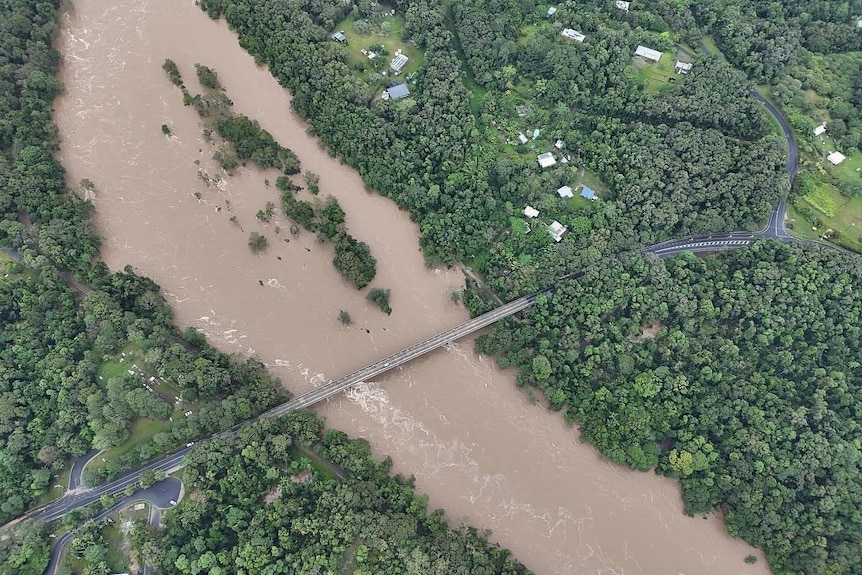 An aerial image of a bridge over a flooded river full of muddy water, greenery on either side.