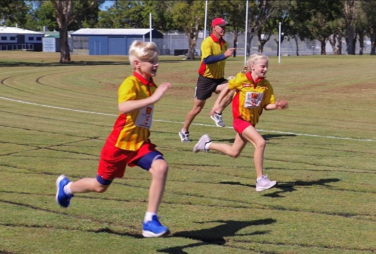Two kids and a man run at a sports oval