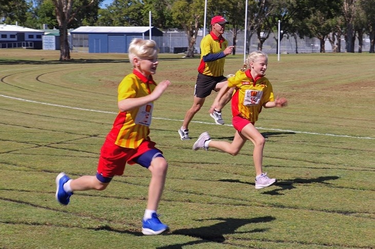 Two kids and a man run at a sports oval