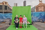 Three women pose at a photoshoot in front of construction fencing
