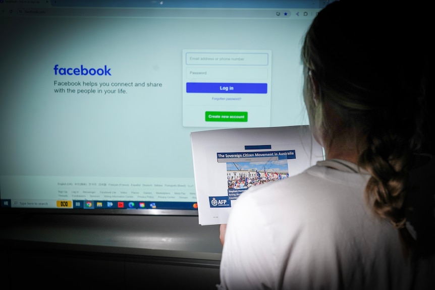 A woman holding an AFP report into the sovereign citizen movement while looking at the Facebook login screen