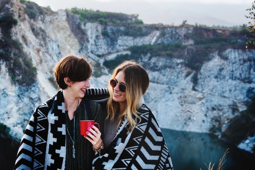 Two women chat while wrapped in a blanket to depict information on how to switch up predictable, routine sex.