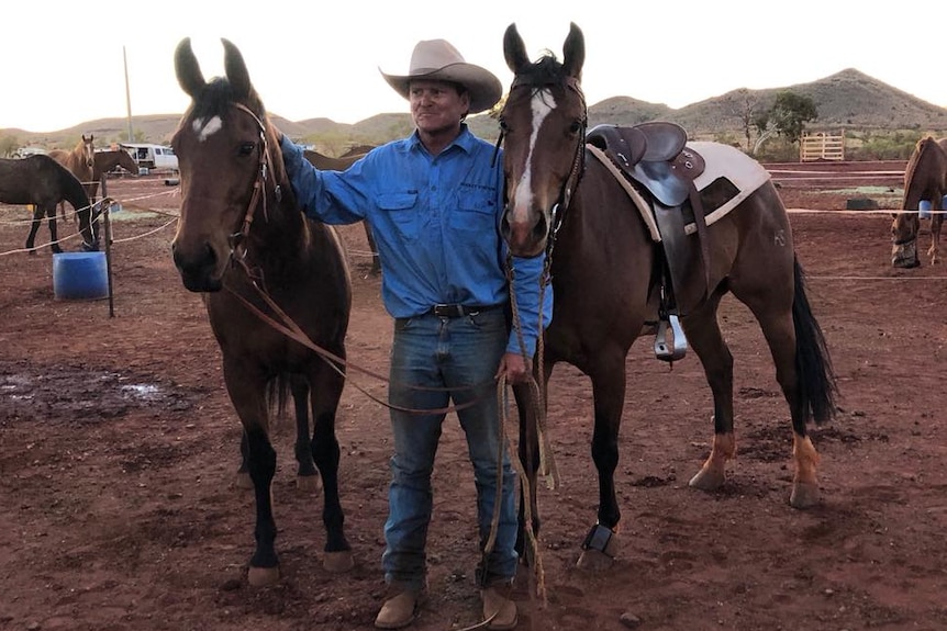 A man stands in a dirt paddock flanked by two horses.