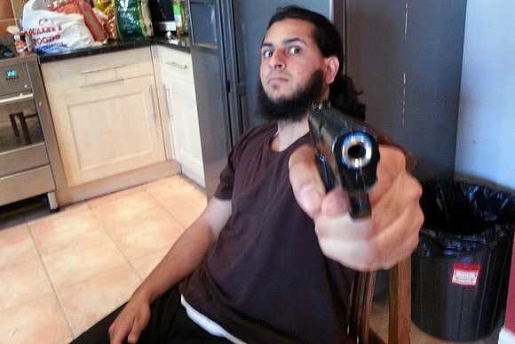 Haseeb Hamayoon points a handgun at the camera with a menacing look on his face.