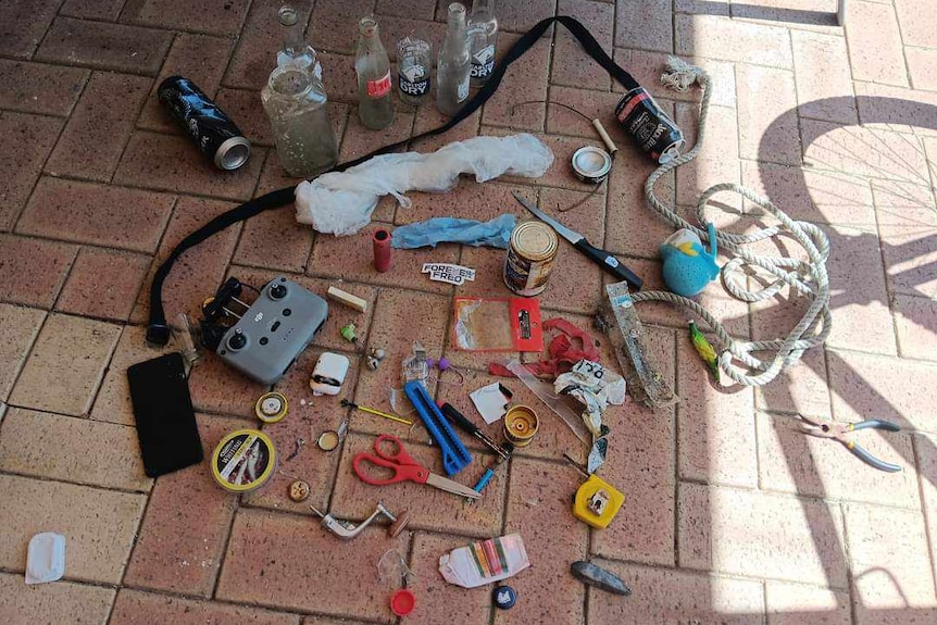 A collection of litter including a drone remote, beer bottles, scissors, a phone, knife and rope.