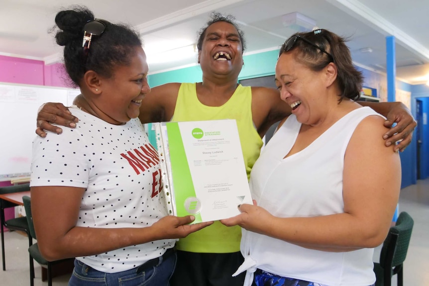 Aboriginal woman laughing with her arm around two other women who are smiling and holding a certificate.