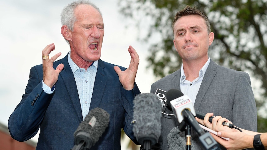 Dickson has his eyes closed, his mouth wide open and both hands raised next to his face. Ashby's lips are pursed.