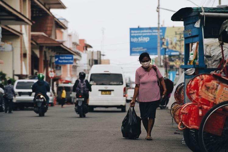 A woman holding a plastic bag walks down a street in Indonesia