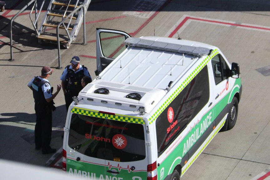 Police talk next to an ambulance parked on an airport tarmac.