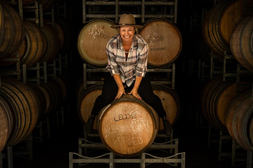 a woman straddles a wine barrel inside a wine cellar