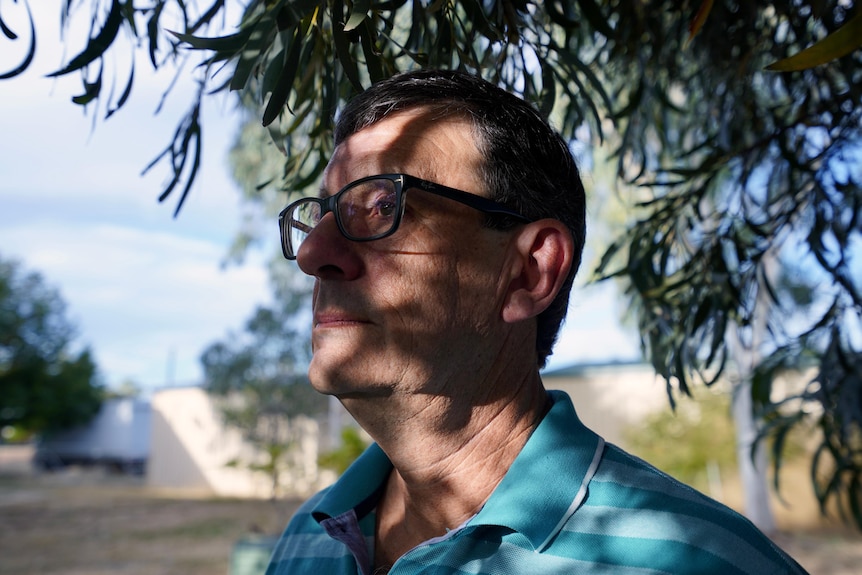 A man wearing glasses with shadows on his face staring into the distance.