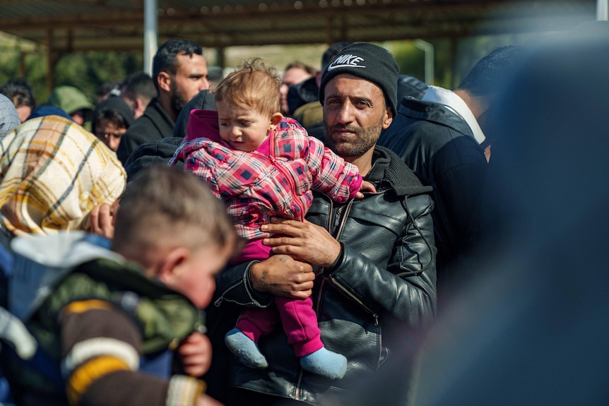A man holds a child in the crowd at the Syrian-Türkiye border.
