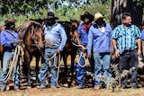 A group of five stockmen stand in front of their horses