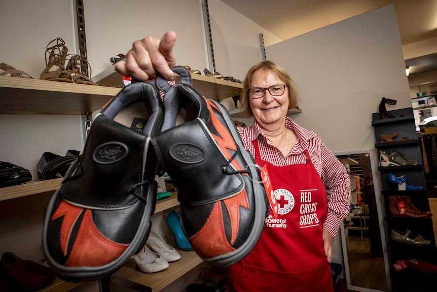 A charity shop  retail manager holds a pair of unique giant shoes for sale