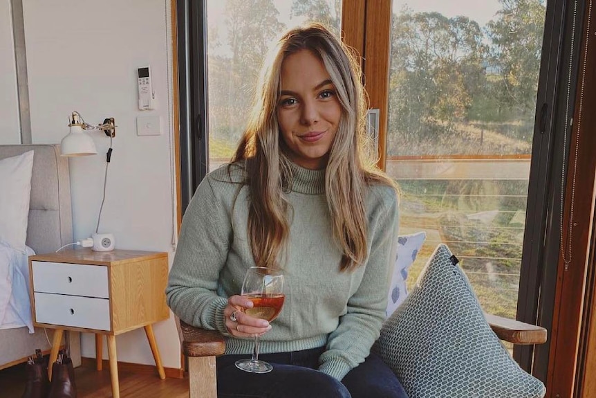 A young woman sits on a chair while holding a glass of wine.