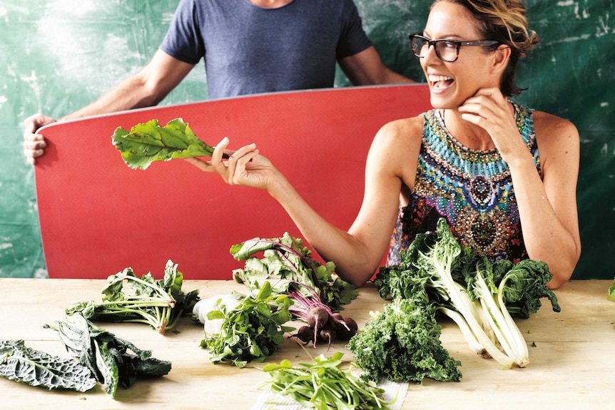 A woman smiles widely, holding a piece of silverbeet.