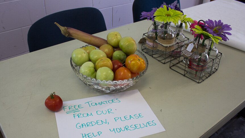 Green, orange and red tomatoes sit in a crystal bowl beside pink, purple and green gerbras and a sign that reads 'Free tomatoes'