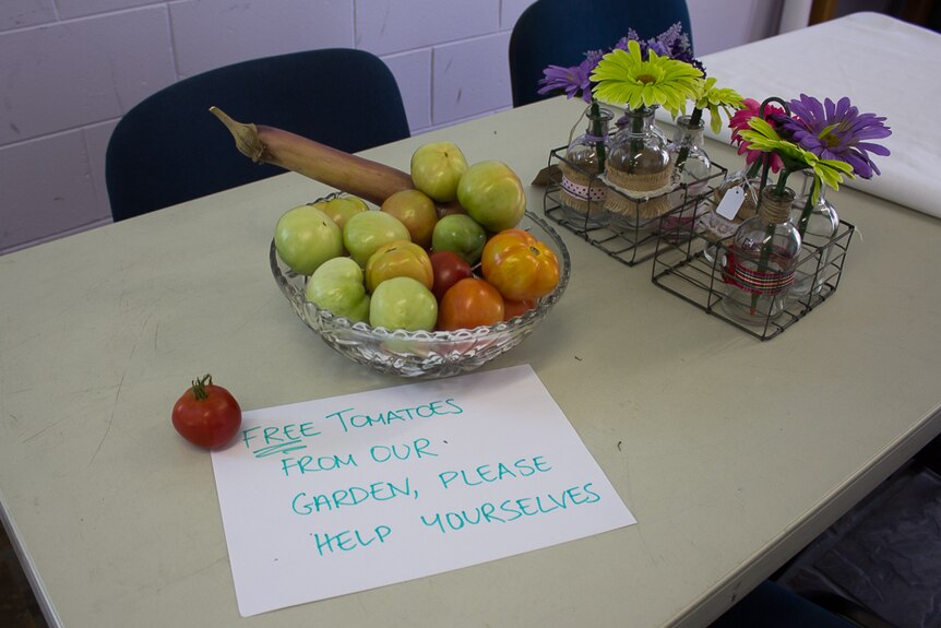 Green, orange and red tomatoes sit in a crystal bowl beside pink, purple and green gerbras and a sign that reads 'Free tomatoes'