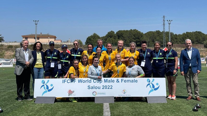 A female soccer team wearing yellow and green uniforms poses with medals during a ceremony