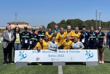 A female soccer team wearing yellow and green uniforms poses with medals during a ceremony