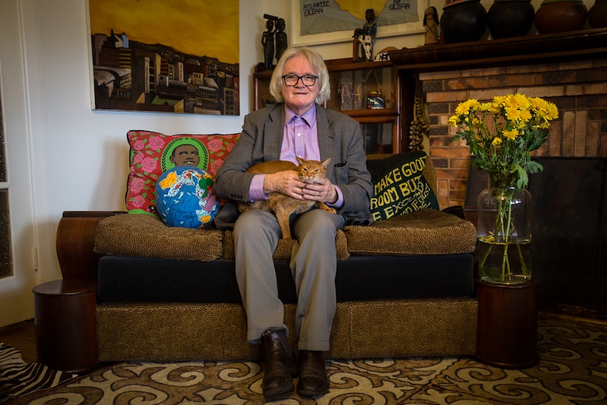 Artist and Theatre Royal's ex-cinema manager Les Thornton sitting on his couch holding his cat.