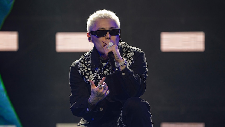 A young Chinese man with rings and bleached blonde hair sings into a microphone onstage.